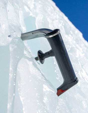 A close-up shot of a modern ice axe providing a secure anchor in a vertical wall of glacial ice.の素材