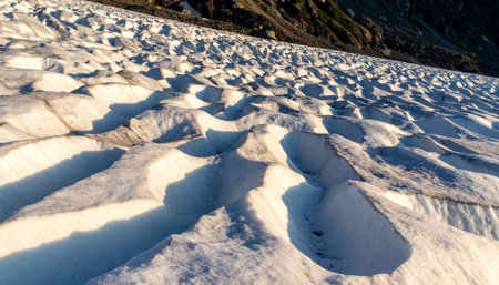 As the sun dips low, its golden rays cast long, dramatic shadows across the undulating surface of a vast glacier.の素材