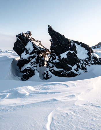 In a vast, silent expanse of untouched snow, an ancient volcanic rock stands cleaved in two, a testament to the immense geological forces that shaped this frozen landscape.の素材