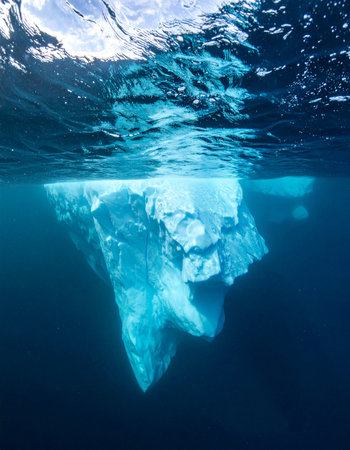 A stunning split-shot view reveals the immense, hidden mass of an iceberg submerged in the deep blue ocean.の素材
