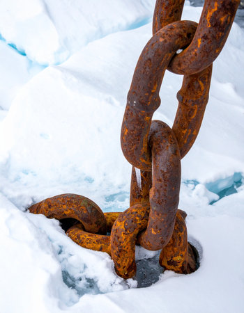 A massive, rust-covered anchor chain is held fast by the unforgiving grip of polar ice.の素材