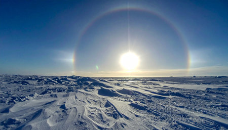 A breathtaking solar halo with vibrant sundogs arches across the clear blue sky, illuminating a vast and desolate frozen wilderness.の素材