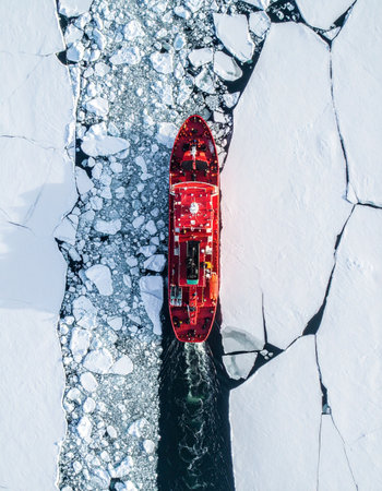 From a stunning top-down aerial perspective, a powerful red icebreaker ship carves a determined path through the vast, frozen expanse of the Arctic.の素材