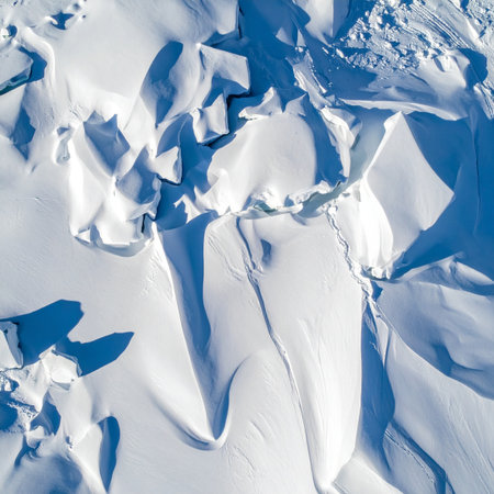 From a high-angle perspective, the winter landscape transforms into a stunning abstract canvas. Deep blue shadows carve through fractured snow and ice, creating a complex geometric pattern.の素材