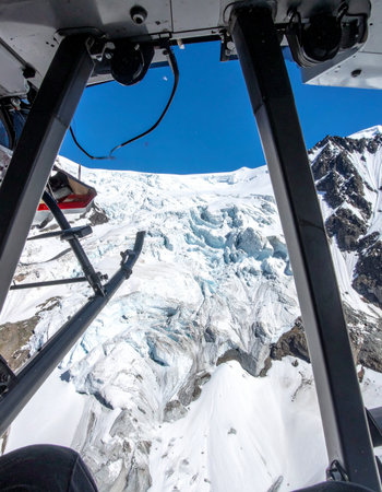 From the cockpit of a helicopter, a breathtaking aerial view unfolds, revealing the immense and cracked surface of a remote mountain glacier.の素材