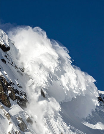 A massive cloud of snow and ice thunders down a steep mountain face in a powerful display of nature's raw force.の素材