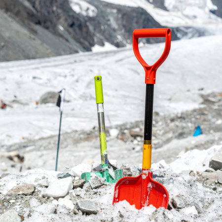 An essential red avalanche shovel stands ready in the rocky, snow-covered terrain of a high-altitude mountain pass.の素材