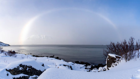 A breathtaking rainbow arches across a dramatic sky, casting a hopeful glow over a serene and frozen arctic coastline.の素材