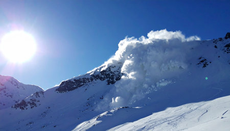 Under a brilliant, clear blue sky, a massive avalanche thunders down a steep mountain face.の素材