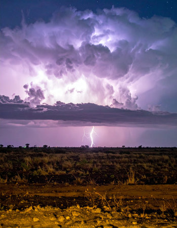 A single, brilliant bolt of lightning tears through the night sky, illuminating a vast, open plain below.の素材