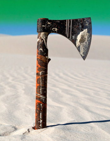 A weathered axe stands alone, embedded in the pristine white sands of a surreal desert.の素材