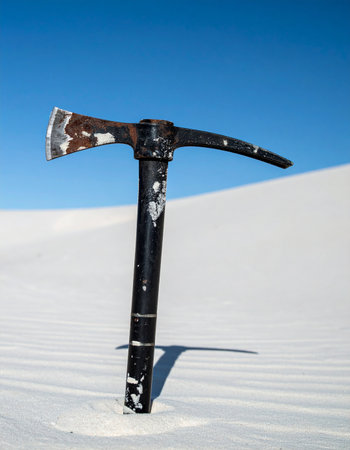 A lone, weathered pickaxe stands planted in a vast, minimalist landscape of pure white sand under a clear blue sky.の素材