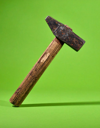 A well-used, rustic hammer with a weathered wooden handle rests against a vibrant green background.の素材