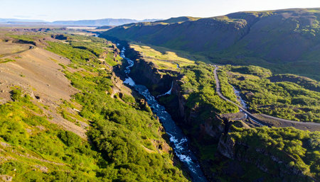 An aerial perspective captures the immense scale and raw beauty of a deep river canyon cutting through Iceland's vibrant green landscape.の素材