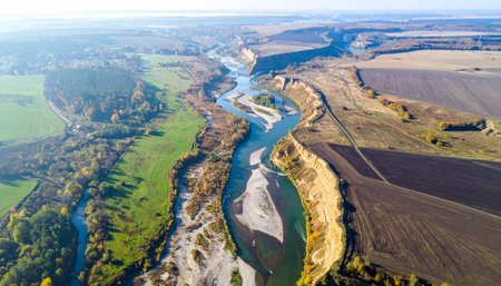 From a breathtaking aerial perspective, a wide river carves its path through a patchwork of vibrant green and earthy brown farmland.の素材