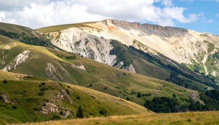 A dramatic white scar, the result of a powerful landslide or ancient geological forces, cuts across the otherwise lush green slopes of a vast mountain range.の素材