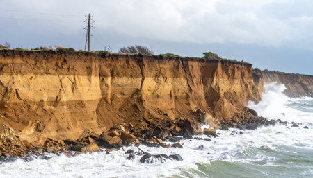 Powerful ocean waves relentlessly crash against a vulnerable earthen cliff, showcasing the dramatic and ongoing process of coastal erosion.の素材