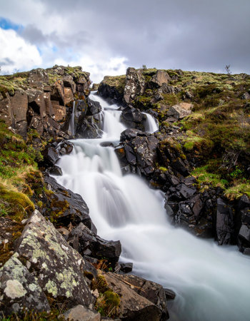 A powerful stream of water carves its path through a rugged, moss-covered canyon in the Icelandic highlands.の素材
