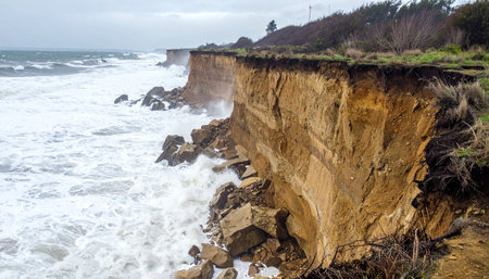 Powerful, churning waves from a stormy sea relentlessly batter the coastline, causing the fragile earthen cliff to crumble and collapse.の素材
