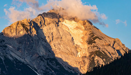 As the day begins or ends, the last rays of golden sunlight kiss the rugged summit of a majestic mountain.の素材