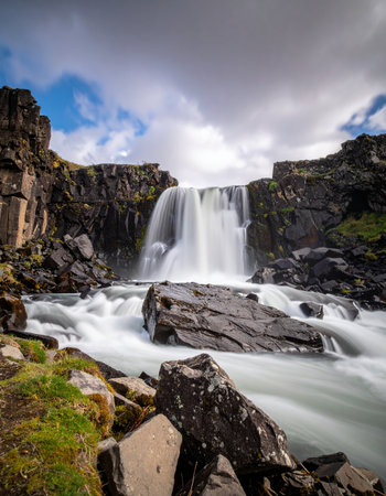 A powerful waterfall carves its path through a rugged, volcanic canyon under a dramatic sky.の素材