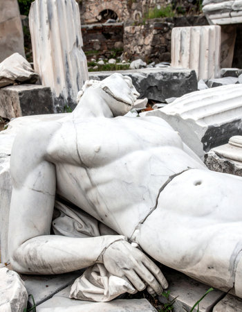 A once-majestic marble sculpture of a classical figure lies broken among the ruins of an ancient civilization.の素材