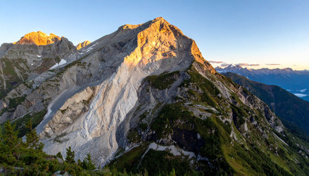 The first rays of dawn kiss the summit of a colossal granite mountain, setting its rugged peak ablaze with a warm, golden light.の素材