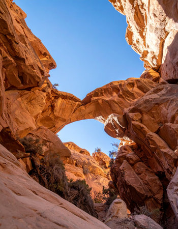Sunlight illuminates a magnificent natural sandstone arch, a testament to the power of erosion, set against a brilliant blue sky.の素材