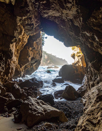 From the cool, dark interior of a hidden sea cave, a stunning view of the bright, sunlit ocean is revealed. Waves crash against the rocky entrance, inviting a sense of adventure and discovery.の素材