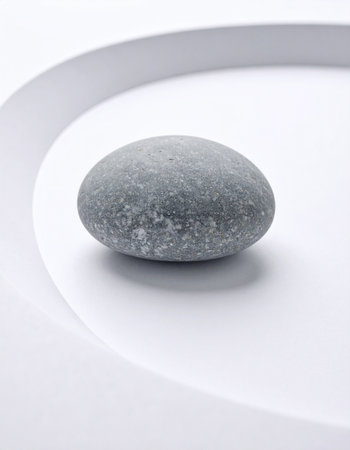 A single, smooth grey stone rests on a clean, curved white surface, creating a powerful symbol of tranquility and focus. This minimalist composition evokes a sense of zen, balance, and quiet contemplation, perfect for concepts related to wellness, meditation, and modern simplicity.の素材