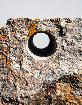 A perfectly circular hole drilled through a rugged, multi-colored mineral rock creates a striking visual contrast. This abstract composition evokes concepts of breakthrough, focused perspective, and a portal to new possibilities, set against a clean, isolated background.の素材