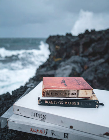 A stack of well-loved books rests against the dramatic backdrop of a stormy sea. Crashing waves and a moody sky create a sense of powerful solitude, perfect for literary escapism and deep contemplation. A quiet moment amidst the raw power of nature.の素材