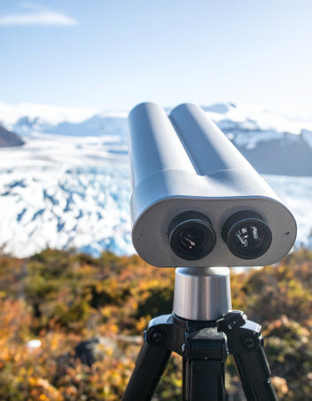 A pair of observation binoculars on a tripod stands ready at a scenic viewpoint, offering a focused perspective on the immense and majestic glacier in the distance. This image captures the spirit of exploration, travel, and the awe-inspiring beauty of remote wilderness destinations.の素材