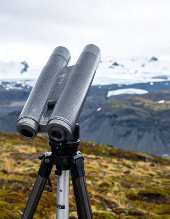Set up at a remote observation point, high-powered binoculars on a sturdy tripod are aimed at the distant, snow-capped mountains. This scene captures a moment of quiet anticipation and exploration in a vast, untouched wilderness, perfect for themes of discovery, travel, and adventure.の素材