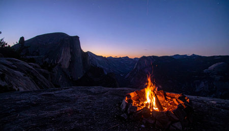 As twilight settles over Yosemite Valley, a warm campfire crackles, casting a cozy glow against the cool granite. The iconic silhouette of Half Dome stands watch in the distance, creating a serene and unforgettable moment of peace and adventure in the wilderness.の素材