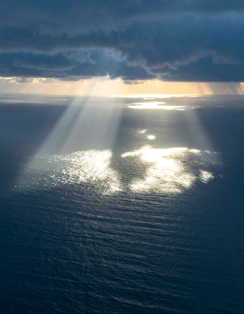 After a period of darkness, dramatic sunbeams break through the stormy clouds, casting a hopeful and divine light upon the calm ocean below. A powerful symbol of breakthrough, faith, and new beginnings.の素材
