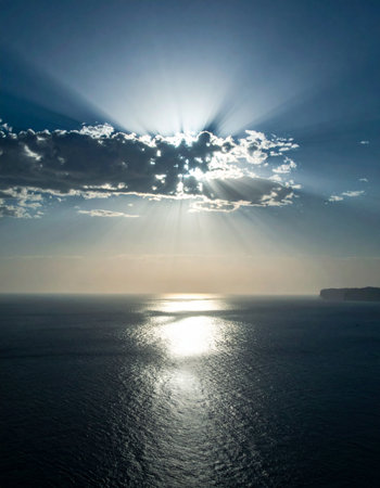 Sunlight bursts through a break in the clouds, sending majestic rays down onto a calm, shimmering ocean. A serene and hopeful scene representing breakthrough, clarity, and new beginnings.の素材