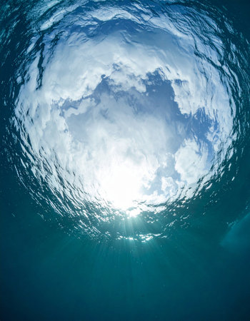From the quiet depths of the ocean, a view upwards towards the light. The sun breaks through the rippled surface, offering a moment of hope, clarity, and serene escape from the world below.の素材