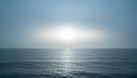 A bright, ethereal light glows on the distant horizon, casting a gentle reflection across the calm, endless ocean. This serene and minimalist seascape evokes a sense of peace, hope, and the quiet mystery of a new beginning or a peaceful end.の素材