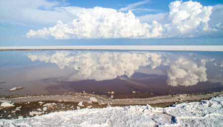 A breathtaking panoramic view of a vast salt flat where the still, shallow water creates a perfect mirror, reflecting the dramatic white clouds and blue sky. The scene evokes a sense of tranquility, infinity, and otherworldly beauty, a natural wonder where heaven and earth meet.の素材