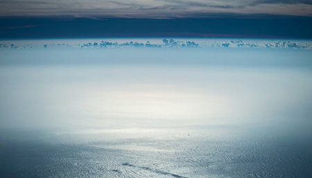 A serene yet powerful view of a vast, frozen ocean stretching to a distant, mountainous horizon. The calm, icy water reflects a moody sky, creating a sense of immense scale, solitude, and the raw, untouched beauty of the polar regions.の素材