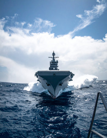 A formidable aircraft carrier slices through the deep blue ocean, its powerful bow creating a massive white wake. Under a vast, cloud-filled sky, this symbol of naval strength and technological prowess embarks on a mission, projecting power and ensuring maritime security across the globe.の素材
