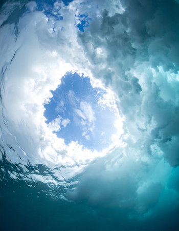 From beneath the turbulent surface, a swirling vortex of water parts to reveal a serene patch of blue sky and clouds. A powerful and dynamic perspective capturing a moment of clarity amidst the chaos of the ocean.の素材