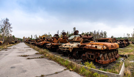 A somber panorama of rusted and destroyed military tanks lined up in a vehicle graveyard. This powerful image captures the devastating aftermath of conflict, symbolizing the cost of war, destruction, and the eventual decay of military power.の素材
