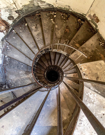 A dizzying top-down view into the abyss of a decaying spiral staircase. Each crumbling step tells a story of forgotten times, leading downward into darkness and mystery. This image captures the eerie beauty of architectural decay and the suspense of exploring abandoned places.の素材
