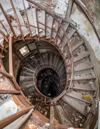 Looking down from the top of a forgotten tower, a decaying spiral staircase twists into a dark, unknown abyss. Each crumbling step tells a story of time, neglect, and the eerie beauty of abandonment, inviting a descent into mystery.の素材