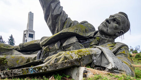 A colossal statue of Lenin, a relic of the Soviet era, lies fallen and forgotten. Covered in moss and weathered by the elements, the once-imposing monument is now a symbol of historical change and the inevitable decay of ideologies, slowly being reclaimed by the quiet persistence of nature.の素材