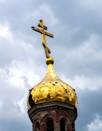 A weathered golden dome, topped with an Orthodox cross, stands resilient against a dramatic, cloudy sky. This powerful image evokes a sense of history, faith, and enduring spirituality through the passage of time.の素材