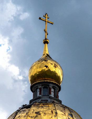 A gleaming golden dome of an Orthodox church reaches towards a dramatic, cloudy sky. The gilded cross at its peak stands as a powerful symbol of faith, hope, and spiritual heritage, reflecting the heavens above.の素材