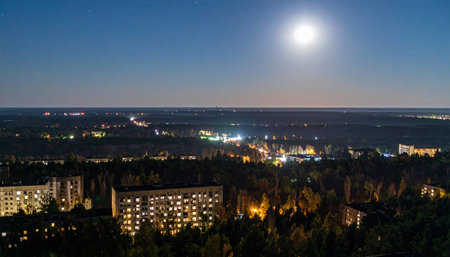 A bright, luminous full moon hangs in the deep blue twilight sky, casting a serene glow over a quiet city. Below, the warm lights of apartment buildings and distant streets create a peaceful urban tapestry as the town settles in for the night.の素材